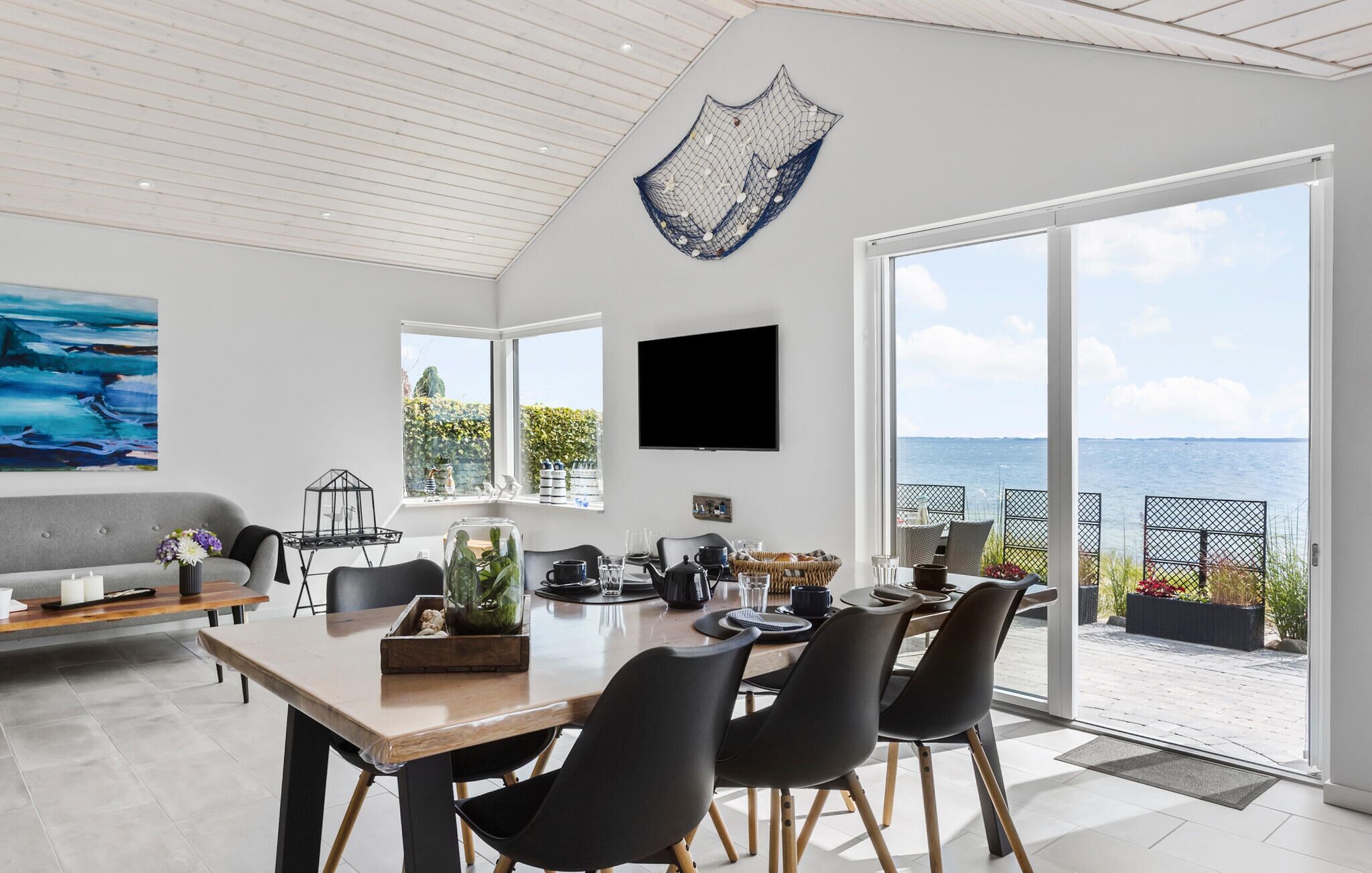 Ein moderner Essbereich mit großem Tisch, schwarzen Stühlen und Meerblick durch große Fenster.