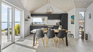 Uma cozinha moderna com uma grande janela com vista para a água, uma área de jantar com mesa e cadeiras, e vista para o mar.