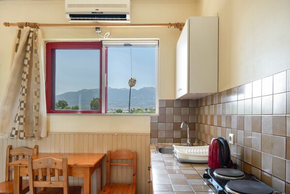 Une cuisine avec une fenêtre, une table, des chaises, un évier et une bouilloire.