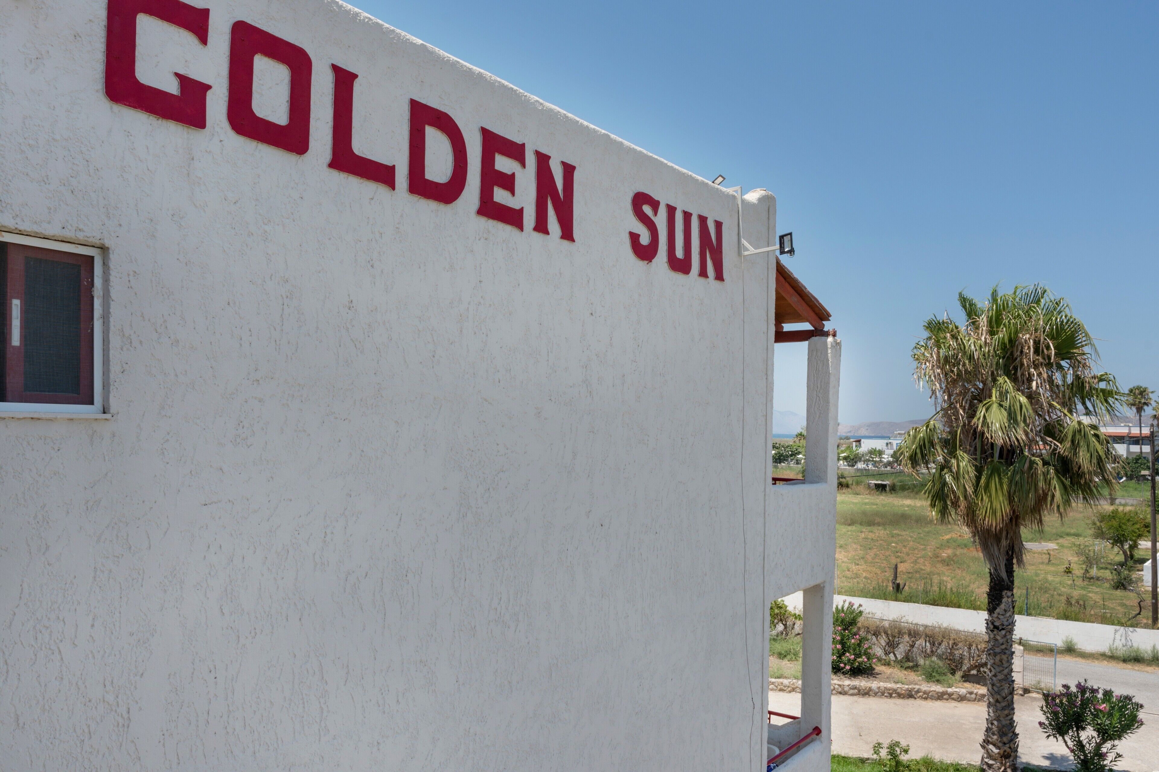 Ein Gebäude mit der Beschilderung 'GOLDEN SUN', einem Fenster und Blick auf eine Palme und die Landschaft.