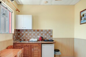 Una cocina compacta con un armario blanco, un lavamanos, un refrigerador pequeño y un salpicadero de azulejos.