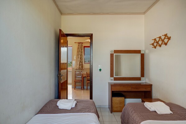 A hotel room with two beds, a desk with a mirror, and a view of a balcony with a chair and curtains.