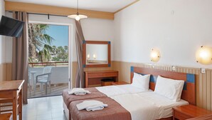 Een hotelkamer met een bed, nachtkastjes, een bureau, een televisie, een balkon met stoelen en uitzicht op palmbomen.