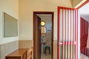 Een kamer met een houten bankje, een deur naar een badkamer en een rood-wit gestreept scherm.