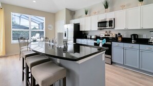Una cocina moderna con armarios blancos, encimera negra y una isla central con taburetes de bar.
