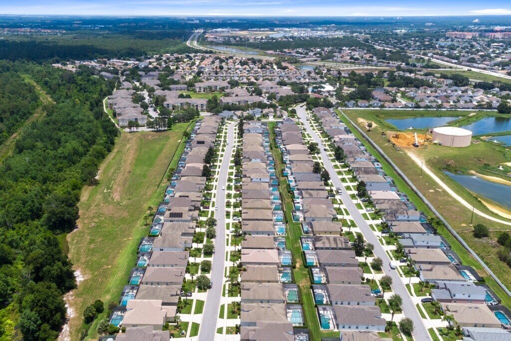 An aerial view of a residential area with a row of houses, a large water tank, and a road curving through the landscape.