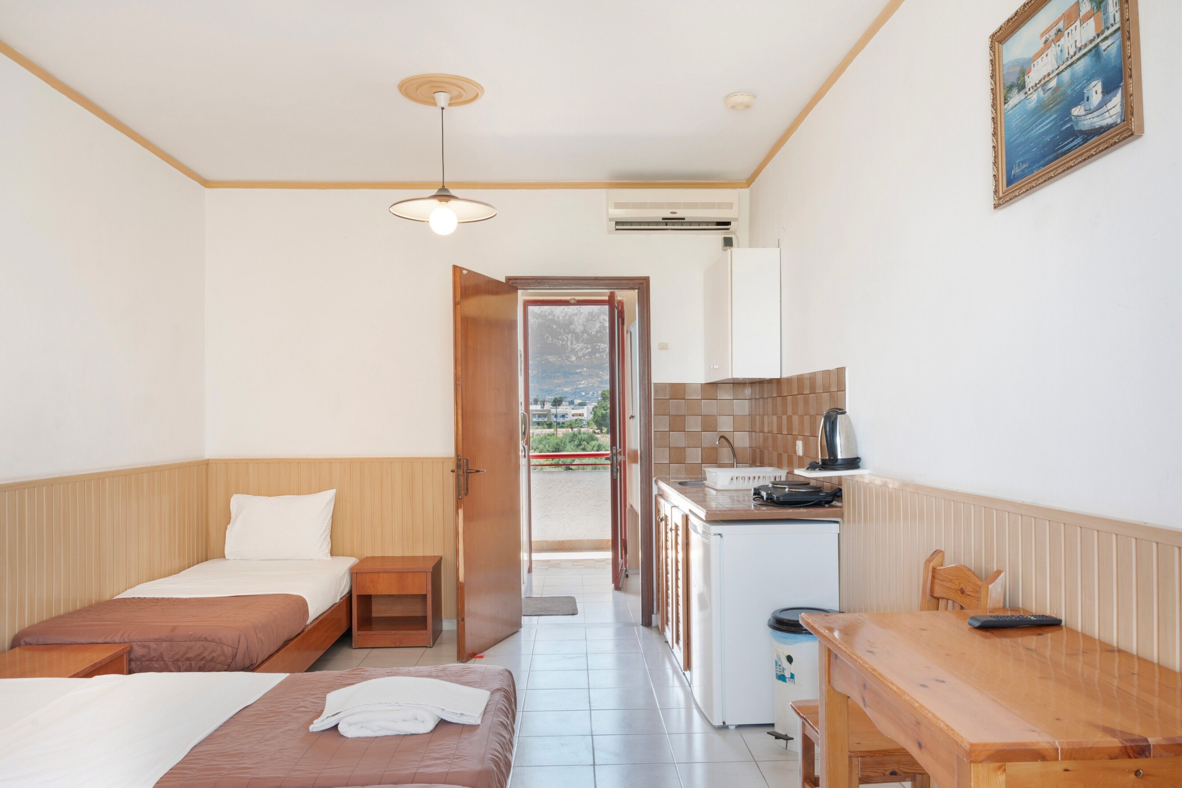 A room with two beds, a kitchenette, a dining table, and a view through an open door.