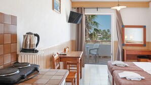 A hotel room with a bed, a table with chairs, a kettle, a television, and a balcony with a view of palm trees. - Studio Apartment 'Golden Sun  6' with Sea View, Shared Pool and Wi-Fi (Tigaki 0)