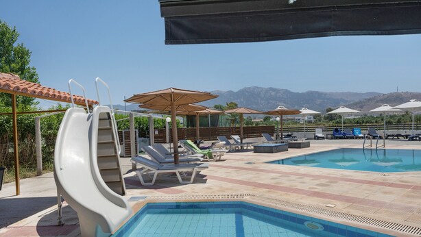 A swimming pool with slides, lounge chairs, umbrellas, and a mountainous backdrop. - Studio Apartment 'Golden Sun  8' with Sea View, Shared Pool and Wi-Fi (Tigaki 0)