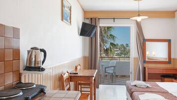 Habitación de hotel con cama, una mesa con hervidor, televisor y balcón con sillas.