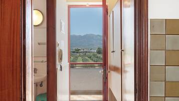 A corridor with a view of mountains, a balcony with a railing, and a door leading to a bathroom.