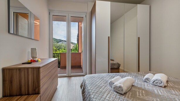 A bedroom with a bed, a wooden dresser, a mirror, and a sliding door leading to a balcony. - Apartment 'My Town Home' with Balcony, Wi-Fi and Air Conditioning (Torri del Benaco)