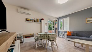 A living room with a sofa, a coffee table, a dining table with chairs, a TV, and an air conditioning unit. - Apartment 'My Town Home' with Balcony, Wi-Fi and Air Conditioning (Torri del Benaco)
