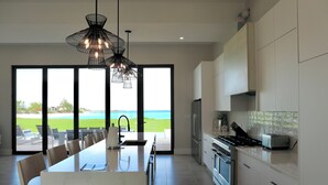 A modern kitchen with a large island, stainless steel appliances, and a view of the ocean. - Coral Cove Villa - New Large 7 Bedroom Modern Luxury Villa + Concierge (George Town)