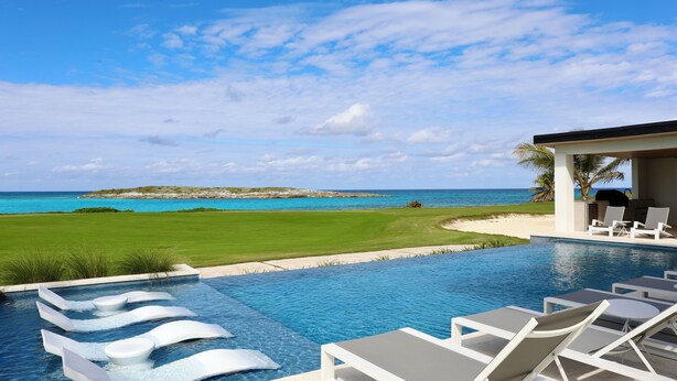 A swimming pool with lounge chairs and a view of the ocean. - Coral Cove Villa - New Large 7 Bedroom Modern Luxury Villa + Concierge (George Town)