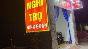 Un edificio con un letrero de neón que dice "NHÀ NGHI TRÓ MINH QUẬN" y una motocicleta estacionada afuera.