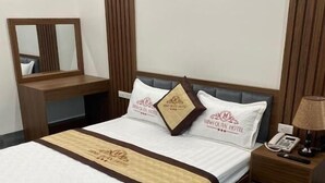 Una cama bien tendida con un cabecero, una mesita de noche con una lámpara y un mueble auxiliar con un teléfono.
