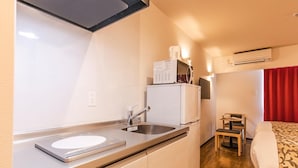 Et kompakt tekøkken med vask, mikroovn og køleskab. Der er et lille spiseområde med en stol og et bord.