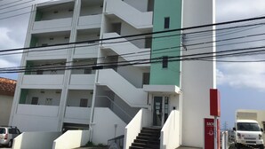 En bygning med flere etager, en grøn og hvid facade, en synlig trappe og et rødt skilt til højre.