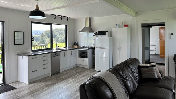 A modern kitchen with white cabinets, a black countertop, and a large window offering a view of the outdoors. - Nibble Nook Farm Cottage (Tapapa)