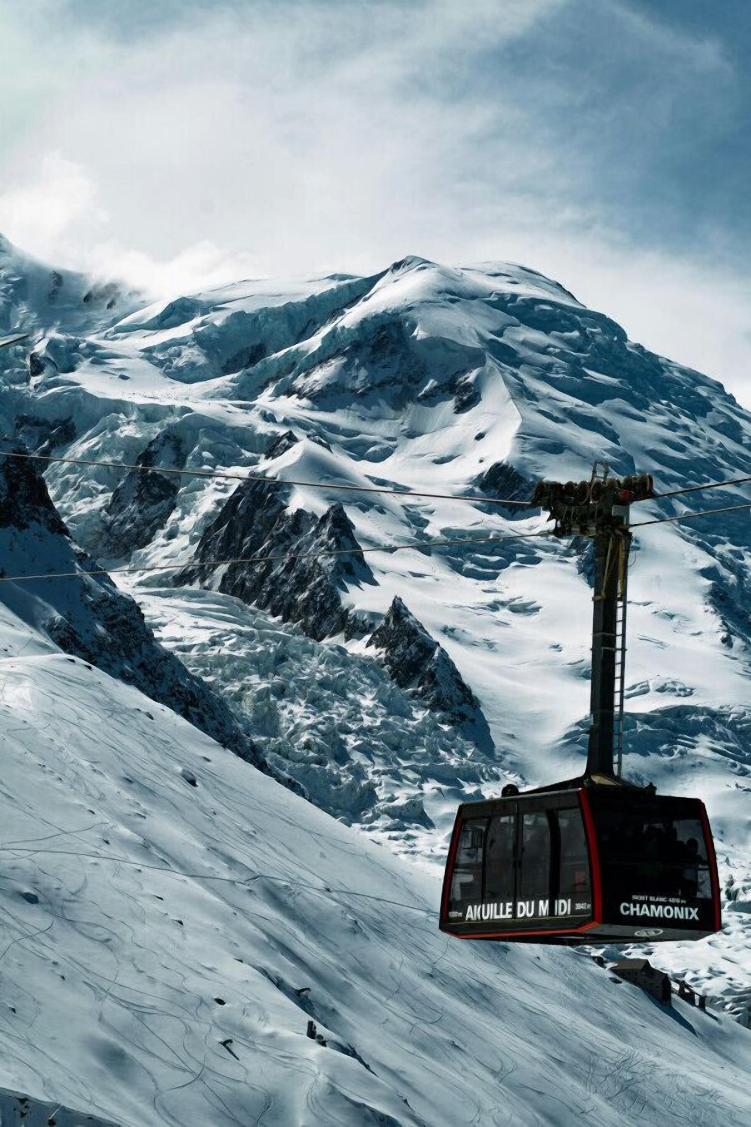 Un teleférico al pie de una montaña nevada con el texto "AKUIILLE DU MADI" y "CHAMONIX".
