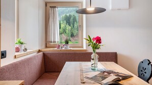 Une pièce avec une table en bois, un banc, une fenêtre donnant sur une forêt et un luminaire suspendu.