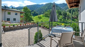 Un balcon avec une table et des chaises, une vue sur un paysage montagneux et un bâtiment doté d’un toit en pente.