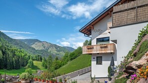Un bâtiment moderne doté d’un balcon, entouré d’une végétation luxuriante et de montagnes.