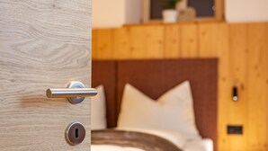 Une porte en bois, dotée d’un trou de serrure et d’une poignée, qui donne sur une chambre à coucher avec une tête de lit en bois et une table de chevet.