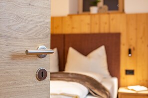 Une porte en bois, dotée d’un trou de serrure et d’une poignée, qui donne sur une chambre à coucher avec une tête de lit en bois et une table de chevet.