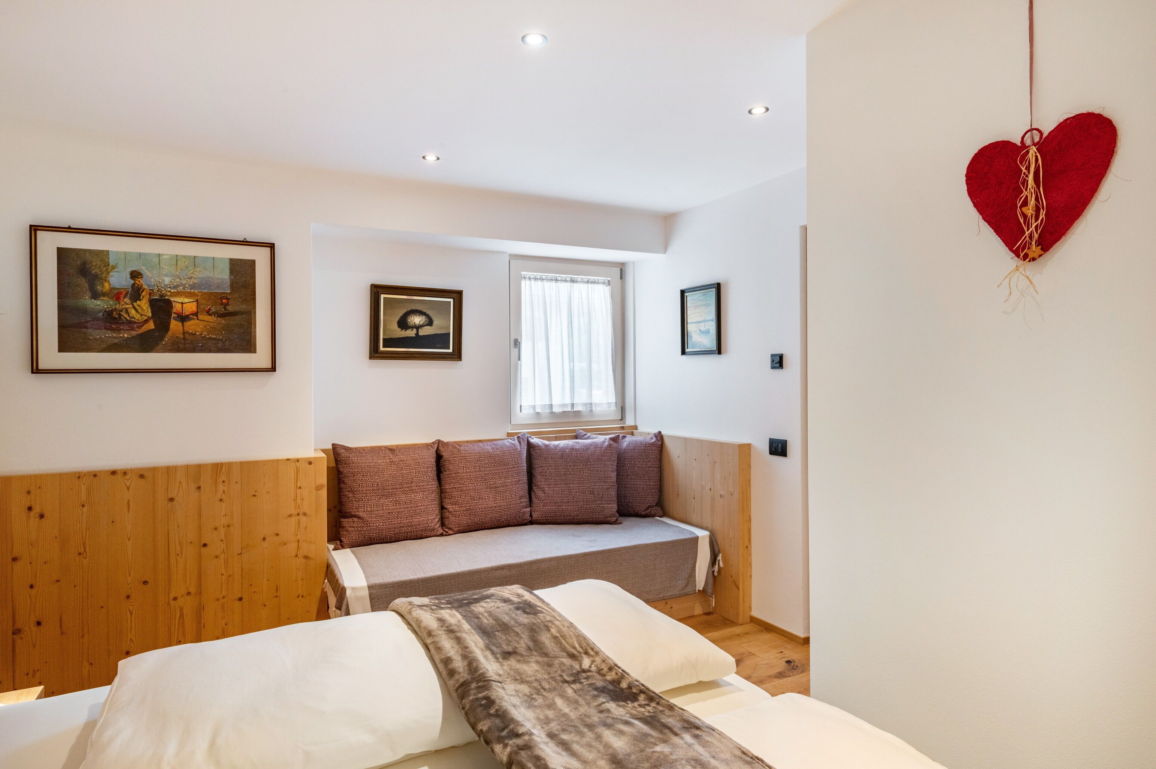 Ein Schlafzimmer mit Holz-Kopfteil, einer Schlafcouch, einem großen Bett und einer roten Herz-Dekoration.