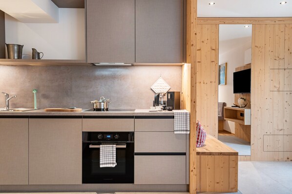 A modern kitchen with a built-in oven, a coffee machine, and a wooden bench.
