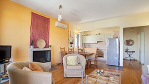 Ein Wohnzimmer mit Sofa, Sessel und Couchtisch, einem Kamin und einer Küche im Hintergrund.