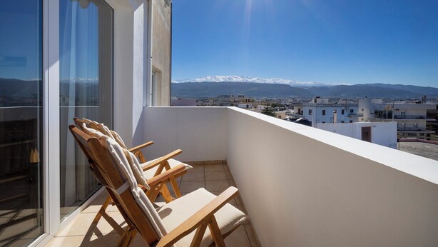 Ein Balkon mit zwei Holzstühlen und Blick auf eine Stadtlandschaft und ferne Berge.