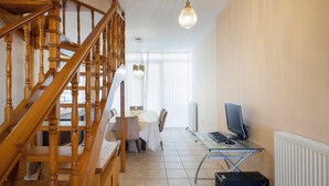 Eine Holztreppe, ein Essbereich mit Tisch und Stühlen sowie ein Computertisch mit Bildschirm und Tastatur.