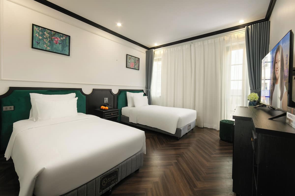 Habitación de hotel con dos camas, un escritorio, un televisor y una ventana con cortinas.