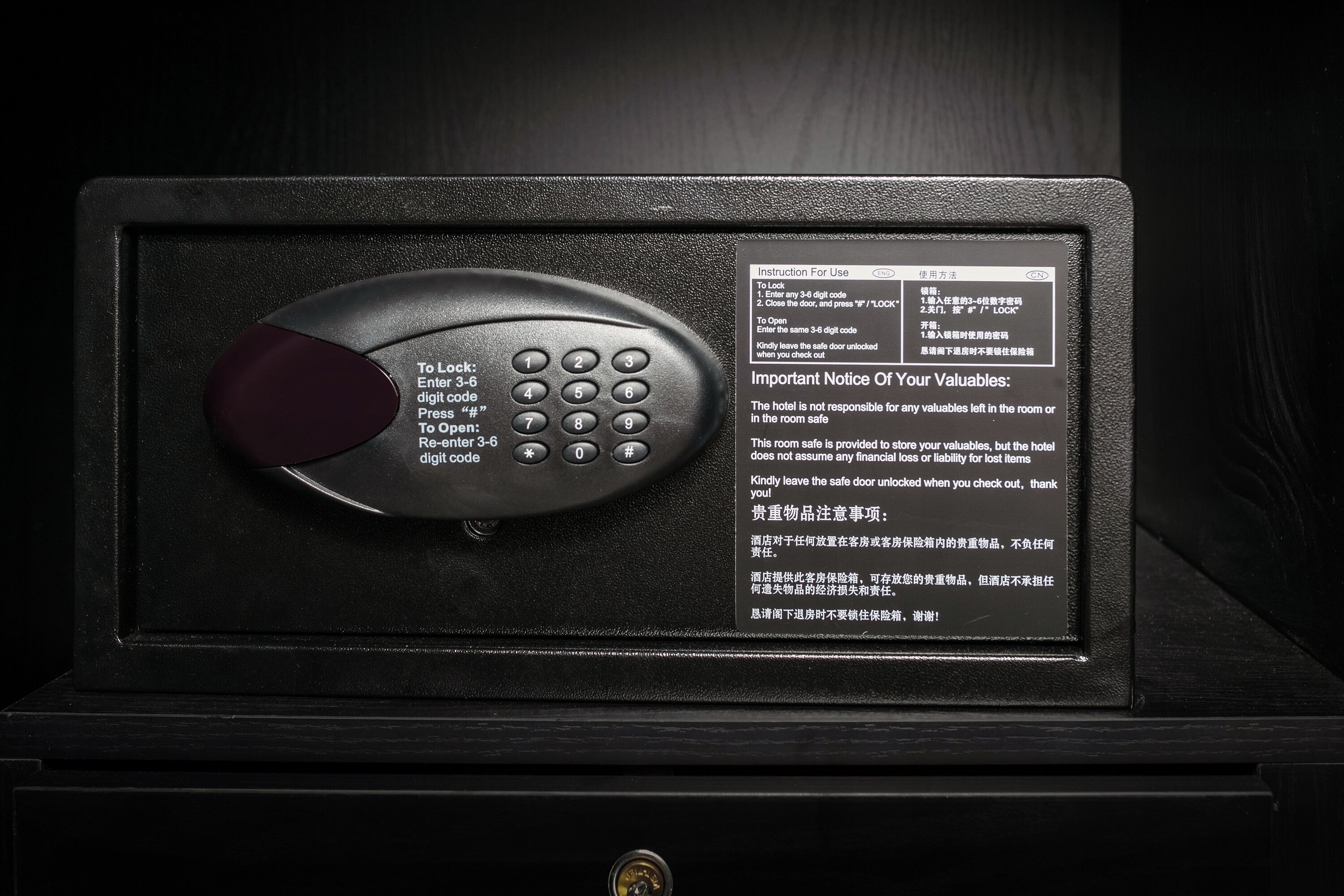 A digital safe with a keypad and a lock button, accompanied by instructions and a notice about valuables.