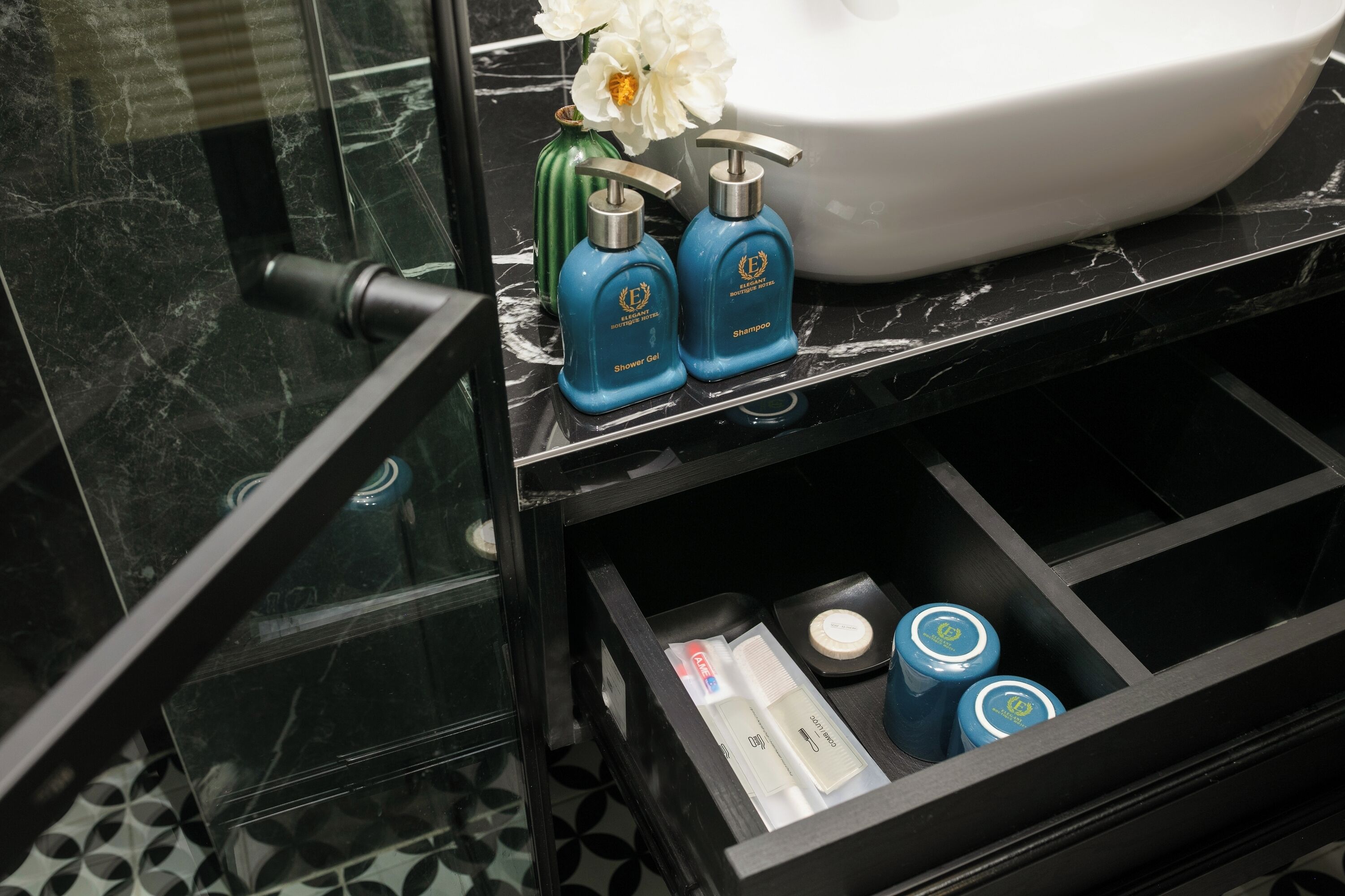 A bathroom with a black marble sink, two blue shower gel bottles, and a glass cabinet containing toiletries.