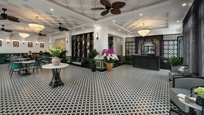 Een hotellobby met een vloer met patroon, groene zitplaatsen, een receptiebalie en plafondventilatoren.