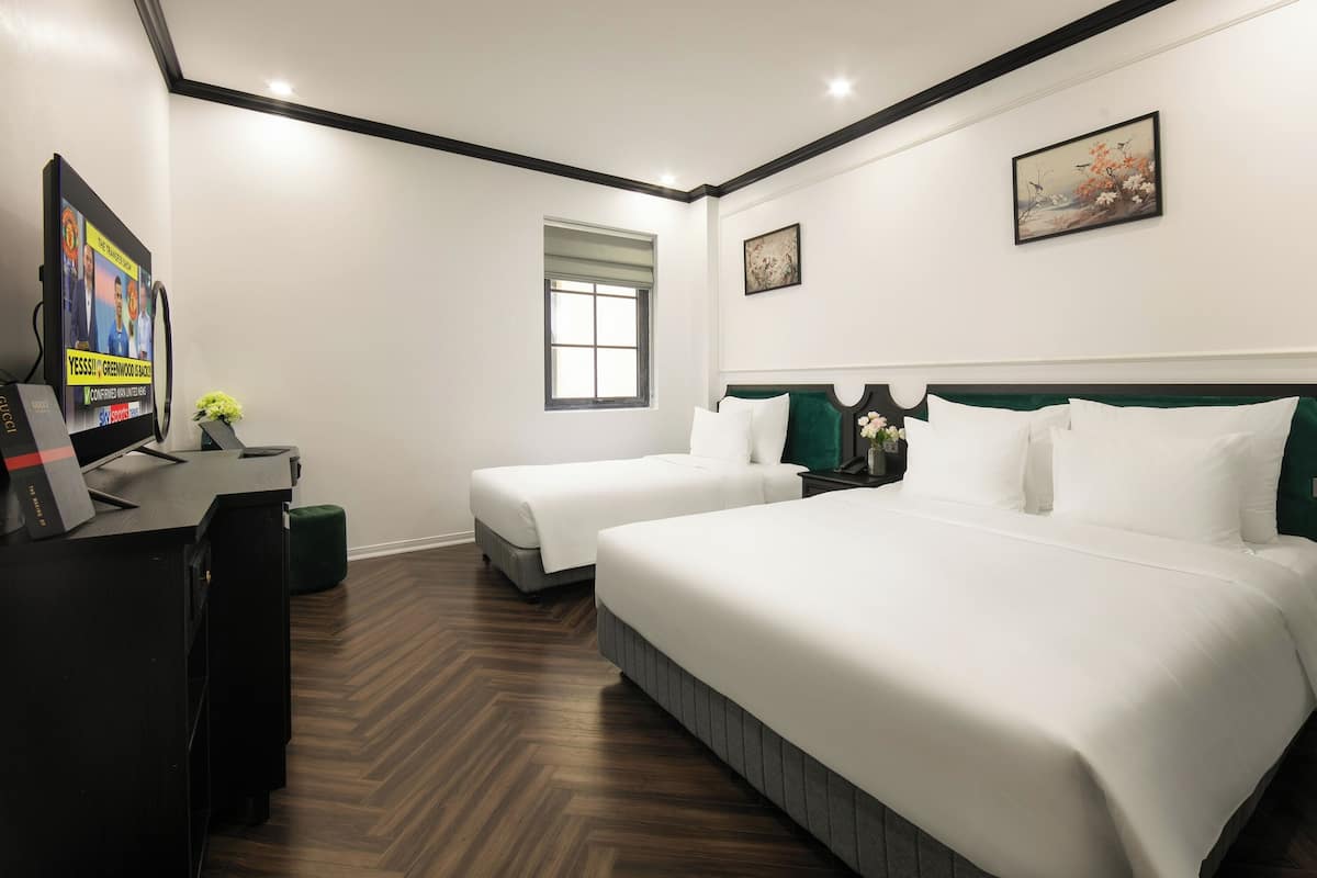 Habitación de hotel con dos camas, un escritorio con computadora, una ventana y obras de arte en las paredes.