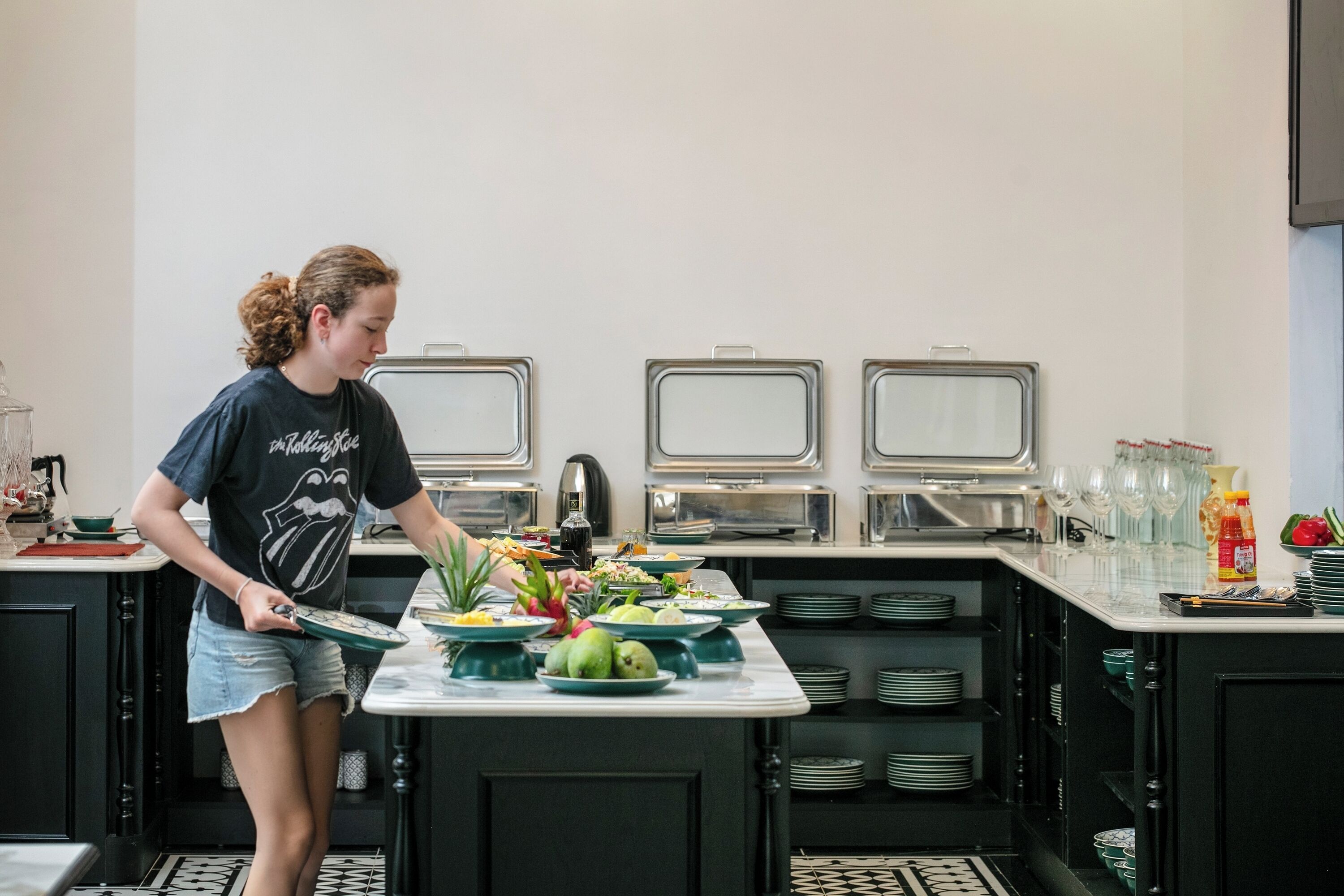 A person serving food at a buffet table in a modern kitchen with black cabinets and white countertops.