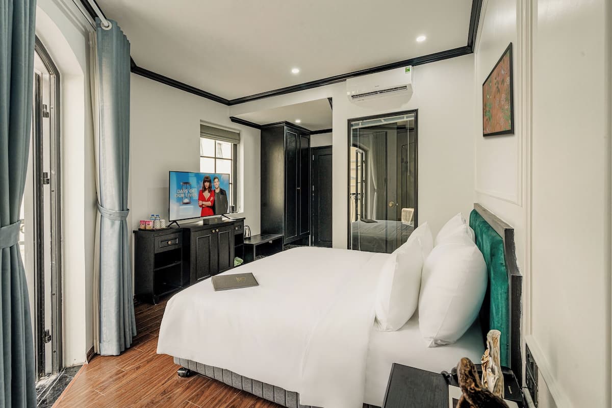 Habitación de hotel con una cama grande, un escritorio con computadora, un espejo y una ventana con cortinas.