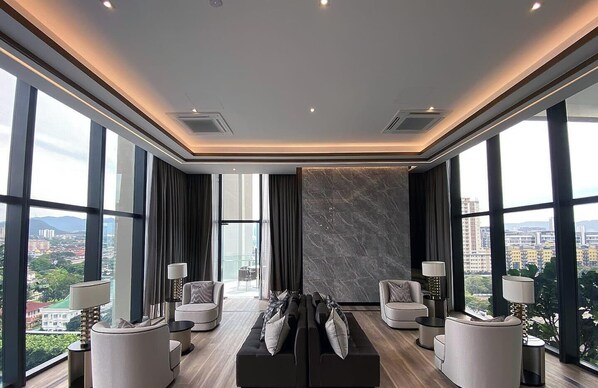 Un salon moderne avec un canapé noir, deux fauteuils et une table basse. De grandes fenêtres offrent une vue sur la ville.