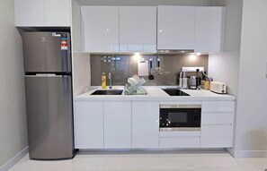 Une cuisine moderne avec des meubles blancs, un réfrigérateur en acier inoxydable, un four encastré et un évier équipé d’un égouttoir à vaisselle.