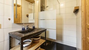 Une salle de bain moderne avec un lavabo en marbre noir, un meuble-lavabo en bois et une douche à parois de verre.