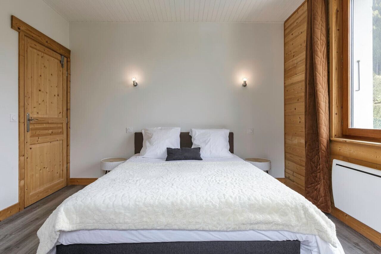 Un dormitorio con una cama grande, un armario de madera, dos mesitas de noche y una ventana con cortinas.