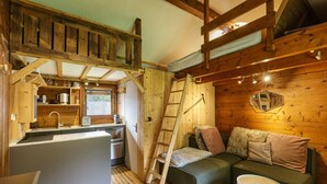 A compact cabin with a kitchenette, a loft bed, and a cozy seating area.