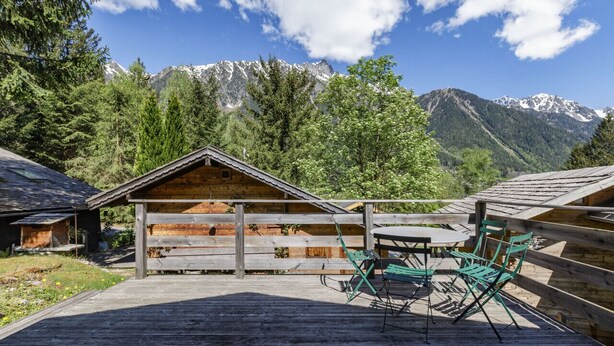 A wooden deck with a table and chairs, surrounded by a wooden fence, overlooking a mountainous landscape.