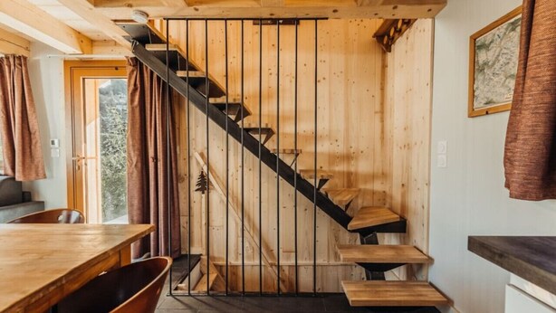 A wooden staircase leading to a second floor, a dining area with a wooden table and chairs, and a framed picture on the wall.
