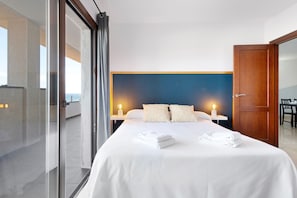 Habitación de hotel moderna con una cama grande, dos mesitas de noche con lámparas, una puerta de madera y vistas a través de una puerta de cristal.